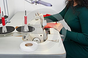 Young tailor using professional overlock sewing machine in workshop studio. Equipment for edging, hemming or seaming