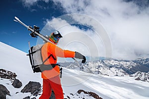 A young tall professional skier holds his skis while standing high in the mountains and looks at the snow-capped peaks.