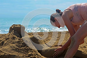 Young tanned girl in a bathing suit close-up on the beach sculpts sand sculpture of sand, a girl lying on the beach in summer