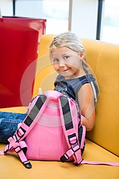 Young tanned girl sitting in airport lounge with her small pink bag, waiting for a flight