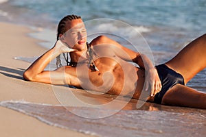 Young tanned man lying on sand at sea water edge and enjoying sunshine