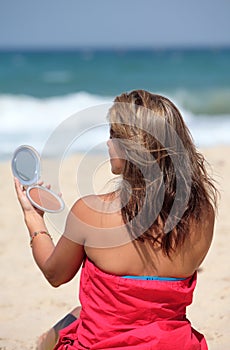 Young tanned woman putting make up on whilst on the beach