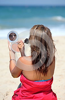 Young tanned woman putting make up on whilst on the beach