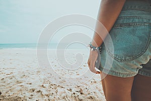 Young tanned woman standing relax on a tropical beach. Blue sea in the background.