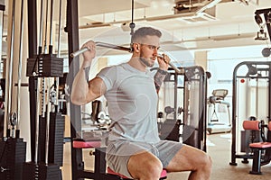 Young tattoed man is doing exercise for back on training apparatus in gym