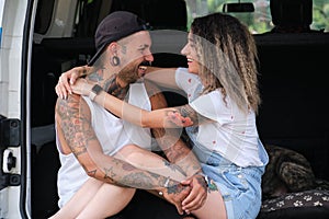 Young tattooed couple smile, hug and look each other in the back of the van.