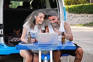 Young tattooed couple smile and talk in a laptop video call during a van trip.