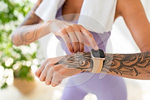 Young tattooed woman looking at activity fitness tracker during workout break, checking heart rate and burned calories