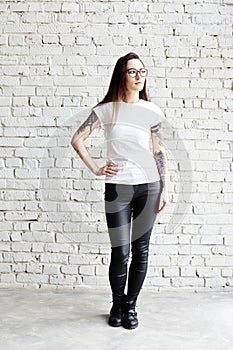 Young tattooed woman wearing blank t-shirt, standing in front of brick wall in loft.