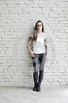 Young tattooed woman wearing blank t-shirt, standing in front of brick wall in loft.