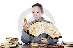 The young TCM pharmacist holds a folding fan to observe the medicine bottle in his hand