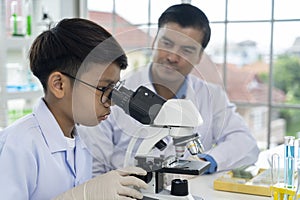 Young teacher and boy use microscope in science class at laboratory