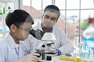 Young teacher and boy use microscope in science class at laboratory