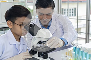 Young teacher and boy use microscope in science class at laboratory