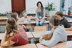 teacher in denim overalls sits on a bench and advises after-school workshops at school photo