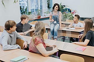 Young teacher in denim overalls sits on a bench and advises after-school workshops at school