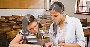 Young teacher guiding schoolgirl while teaching and explaining in classroom at school