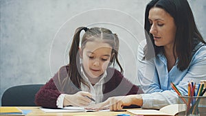 Young teacher helping child writing lesson or mother and daughter learning to write, mother teaching little girl