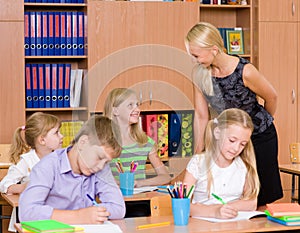 Young teacher helps students of primary school in the exam photo