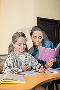 young teacher reading book near girl