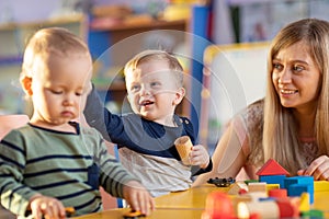 Young teacher and toddlers playing with building blocks toy at kindergarten