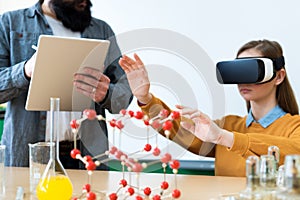 Young teacher using Virtual Reality Glasses and 3D presentation to teach students in chemistry class. Education, VR, Tutoring.