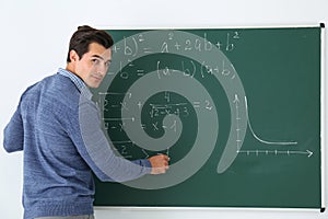 Young teacher writing math formulas on chalkboard
