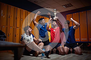 Young team players celebrating first place won, holdin golden trophy and cheering in the locker room