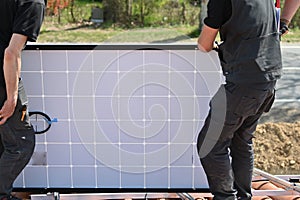 Young technician installing alternative energy photovoltaic solar panels on new house roof  with specialized tools