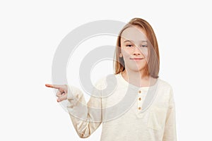 Young teen boy with long hair posing at studio. Guy showing aside at empty space. Emotional portrait of happy teen boy over white