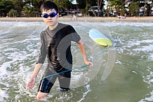 Young teen boy surfer holding rope of soft board, bring it to try again in wave. Rookie teenager surfboard student playing on