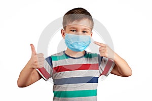 Young teen boy wearing medical mask shows thumbs up and pointing to the mask. Wearing a medical mask is good. Healthcare