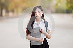 Young teen female Asian university student with bagpack holding laptop in the university campus. Female university student go to u