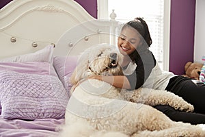 Young teen girl cuddling pet dog on her bed