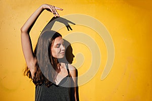 Young teen girl dancing outdoors on yellow wall background in urban area