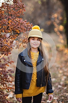 Young teen girl with long blond hair in yellow sweater, hat and leather jacket posing in the autumn park. Copy space