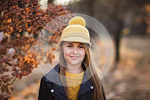 Young teen girl with long blond hair in yellow sweater, hat and leather jacket posing in the autumn park. Copy space
