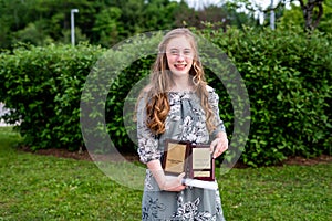 Young teen girl/Middle school student standing in front of a bush/garden after her graduation ceremony while holding a diploma and