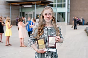 Young Teen Girl/Middle School student standing in front of school with awards and diploma after Grade 8/Middle school graduation c