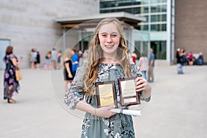 Young Teen Girl/Middle School student standing in front of school with awards and diploma after Grade 8/Middle school graduation c