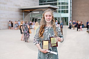 Young Teen Girl/Middle School student standing in front of school with awards and diploma after Grade 8/Middle school graduation c