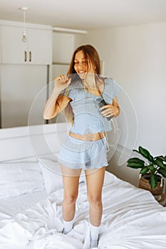 Young teen girl in pajama standing on her bed and singing a song. Cheerful caucasian adolescent girl with headphones