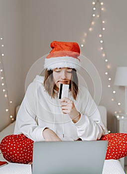 Young teen girl in red santa hat shopping online buying Christmas gifts