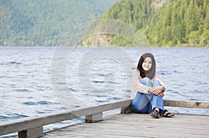 Young teen girl relaxing quietly on lake pier,