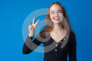 Young teen girl showing a peace symbol with fingers against blue background