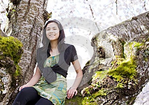 Young teen girl sitting on branches of flowering cherry tree