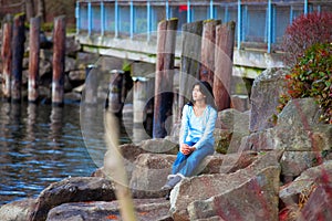 Young teen girl sitting on large boulders along lake shore, looking out over water