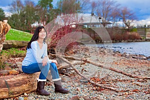 Young teen girl sitting on log along rocky beach of lake