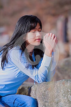 Young teen girl sitting outdoors on rocks praying