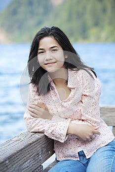 Young teen girl sitting quietly on lake pier